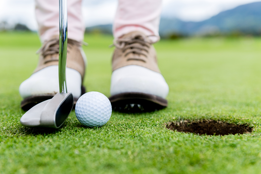 Golf player at the putting green hitting ball into a hole